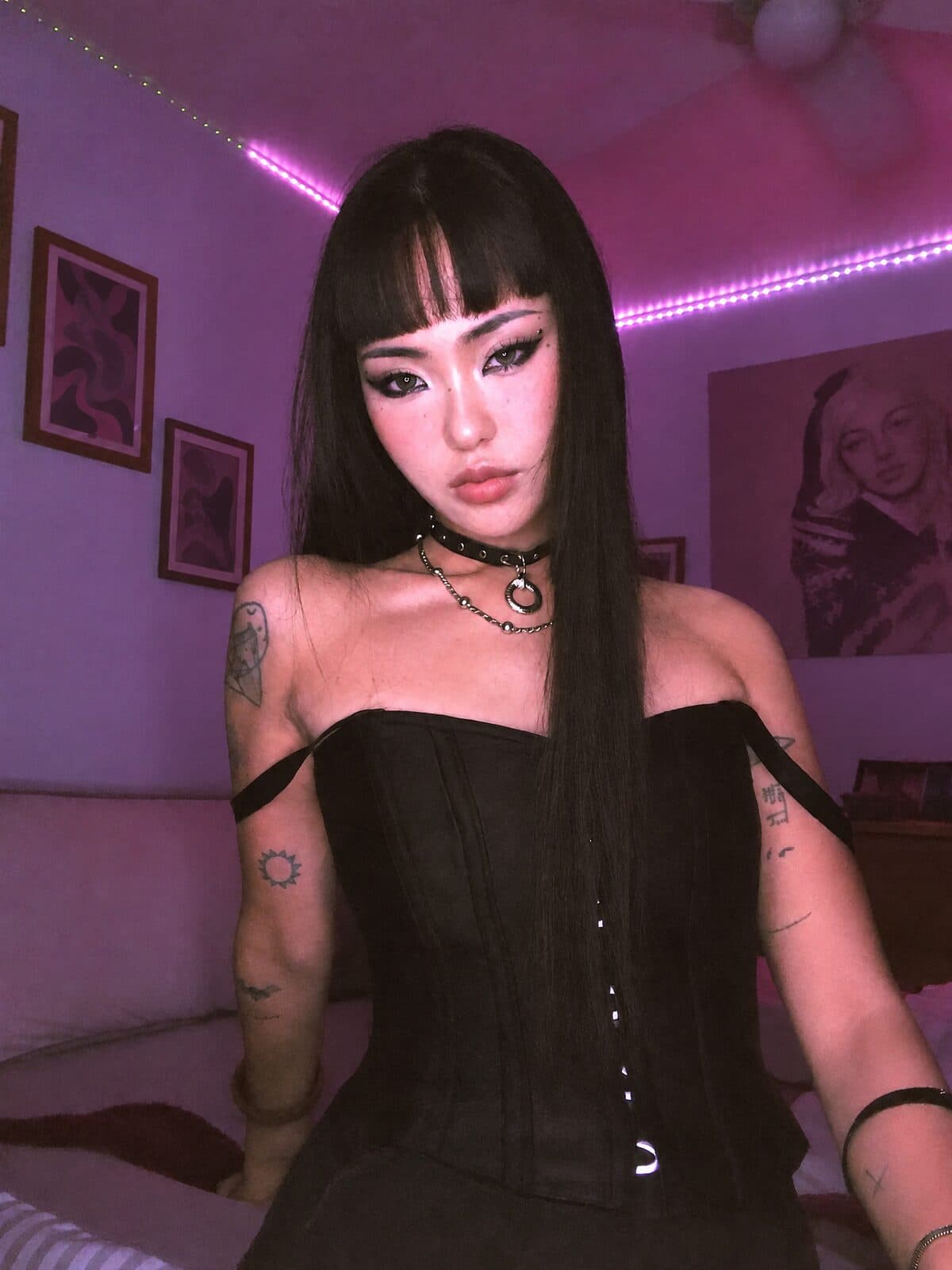 An alt creator with dark hair and tattoos in a purple-lit room
