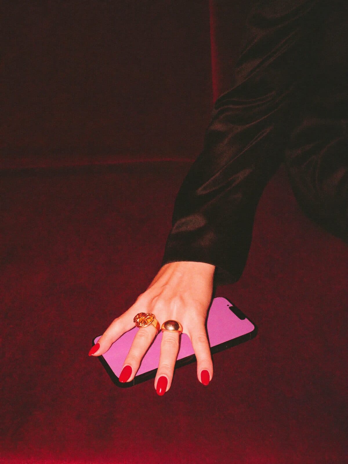 A hand with red nails holding a glowing phone on red velvet