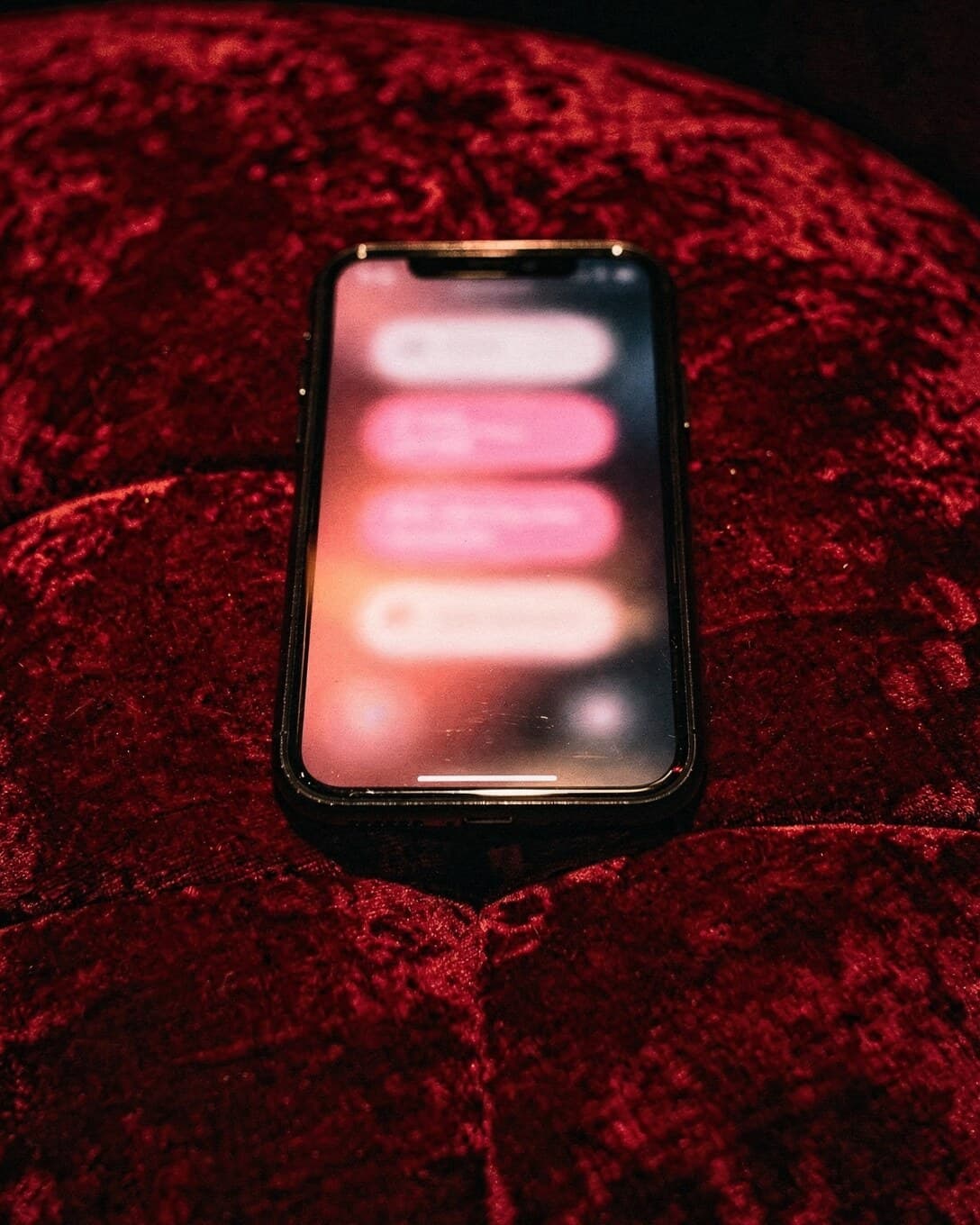 A phone face up on crimson velvet, its screen showing a column of blurred message bubbles